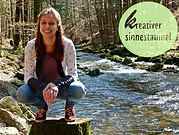 Junge Frau beim kreativen Sinnestaumel in einem Wald mit Fluss, umgeben von Bäumen, kreative Inspiration, Naturerlebnis, Outdoor-Aktivität, nachhaltiges Handwerk.