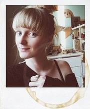 Porträt einer jungen Frau mit blonden Haaren und Zopf, die handgemachte Kunstwerke in einem kreativen Raum präsentiert, ideal für Handmade- und Kunsthandwerks-SEO.