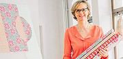 Frau mit Brille und Kurzhaarfrisur hält bunte Stoffe und zeigt handgemachte Quilts, die kreative Handwerkskunst und nachhaltiges Design repräsentieren.