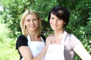 Zwei Frauen mit Schürzen beim Basteln im Grünen, kreative Handwerkskunst bei Handmade Kultur, gemeinsames Hobby, Natur, nachhaltiges Handwerk, DIY, kreative Freizeitgestaltung.