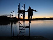 Person balanciert auf einer Leiter am Wasser bei Sonnenuntergang, ruhige Atmosphäre, Natur, Entspannung, Outdoor-Aktivität, Wasser, Abendhimmel, Naturerlebnis, Freizeit, Ruhe.