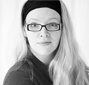 Schwarz-weiß-Fotografie einer Frau mit langen Haaren, Brille und Stirnband, die direkt in die Kamera schaut, mit einem professionellen und kreativen Ausdruck.