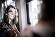 Frau mit Brille und braunem Musterkleid, die an einem kreativen Handwerksprojekt arbeitet, symbolisiert die kreative Atmosphäre von Handmade Kultur.