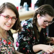 Zwei junge Frauen bei einer kreativen Handwerksaktivität, die handgemachte Kunstwerke in einer Gemeinschaftsveranstaltung präsentieren, mit Fokus auf Handarbeit und Kreativität.