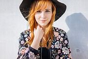 Junge Frau mit rotem Haar, schwarzem Hut und floralem Jacke, die kreative Handwerkskunst und Mode bei Handmade Kultur präsentiert.