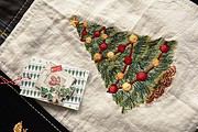 Detailaufnahme eines handgestickten Weihnachtsbaums mit roten und goldenen Perlen auf Stoff, passend für festliche Dekorationen und Weihnachtsgeschenke.