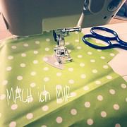 Nähmaschine näht auf grünem Stoff mit weißen Punkten, daneben liegen blaue Schere und ein Herz aus Stoff, symbolisiert kreatives Handarbeiten bei HANDMADE Kultur.