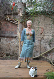 Frau in handgefertigtem Kleid mit Katze auf Holzterrasse, umgeben von Natur und künstlerischer Dekoration, bei HANDMADE Kultur. Perfekt für DIY- und Kunstliebhaber.