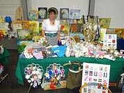 Künstlerin präsentiert handgemachte Kunstwerke und kreative Produkte bei der HANDMADE Kultur, umgeben von bunten Gemälden und handgefertigten Dekorationen.