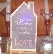 Holzschild mit Aufschrift "This Home is filled with endless LOVE" in Pastellfarben, dekoriert mit Kerzen und Glasvasen, handgemacht, für gemütliches Zuhause.