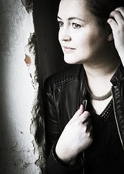 Elegante junge Frau mit dunkler Lederjacke und Perlenkette, nachdenklich blickend, in urbaner Umgebung, für Handmade Kultur SEO optimiert.