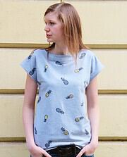Junge Frau trägt ein hellblaues Top mit Ananas-Muster, casual Style, vor einer gelben Wand, Fokus auf Mode und Handarbeit, sommerlich, trendig, feminin.