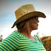 Frau trägt einen großen Strohhut und ein gestreiftes Shirt, umgeben von Natur, bei Handmade Kultur Veranstaltungen, Fokus auf handgemachte Mode und Accessoires.