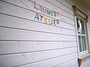 Bunte Buchstabenbanner mit 'Kreativ Atelier' an einer weißen Holzfassade, symbolisiert handgemachte Kreativität und DIY-Projekte bei HANDMADE Kultur.