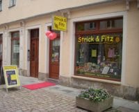 Handarbeitsgeschäft 'Strick & Fitz' mit bunten Wolle und Strickzubehör im Schaufenster, Außenansicht in einer Fußgängerzone, einladend für Handarbeitsliebhaber.