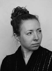 Schwarz-weiß Porträt einer Frau mit hochgestecktem Haar, nachdenklich blickend, in dunkler Kleidung, Ausdruck von Kreativität und Handwerkskunst.