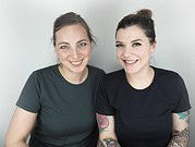 Zwei lachende Frauen mit Tattoos präsentieren kreative Handwerkskunst bei HANDMADE Kultur, einer Plattform für handgemachte Produkte und DIY-Projekte.