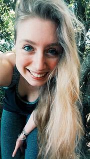Lächelnde junge Frau mit langen blonden Haaren in einem grünen, bewaldeten Umfeld, ideal für Natur- und Lifestyle-Themen bei Handmade Kultur.