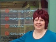 Freundliche Frau mit roten Haaren vor einer Glaswand mit handgeschriebenen Kursangeboten, symbolisiert kreative Handarbeit und Kurse bei HANDMADE Kultur.