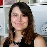 Junge Frau mit braunen Haaren und freundlichem Lächeln, umgeben von kreativen Handwerksmaterialien, symbolisiert Handmade Kultur und kreative Handarbeit.