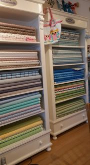 Verschiedene Stoffe und Nähzubehör in einem weißen Regal bei HANDMADE Kultur, ideal für kreative Nähprojekte und handgemachte Textilkunst.