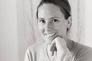 Junge Frau mit freundlichem Lächeln, trägt Ohrringe und einen Pullover, zeigt Kreativität und Handwerkskunst, ideal für Handmade Kultur und DIY-Projekte.