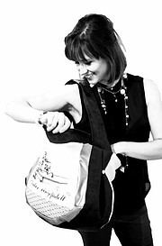 Frau mit dunklem Haar, trägt schwarze Kleidung und Schmuck, öffnet eine Tasche, die mit handgemachten Produkten gefüllt ist, bei Handmade Kultur Veranstaltung.