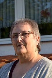 Porträt einer älteren Frau mit Brille und kurzen Haaren, die handgemachte Kunstwerke präsentiert, bei einem Outdoor-Event von HANDMADE Kultur, Fokus auf Kreativität und Handarbeit.
