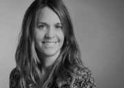 Schwarz-Weiß-Fotografie einer lächelnden Frau mit langen Haaren, die direkt in die Kamera schaut, in einem professionellen Umfeld.