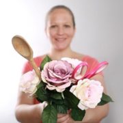 Frau hält einen Blumenstrauß aus Papierrosen mit Bastelwerkzeugen wie Schere, Holzlöffel und Bastelzubehör, kreative Handarbeit und DIY-Projekt.