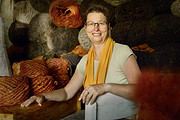 Frau in Wollgeschäft mit bunten Garnrollen, die handgefertigte Strickwaren und Wolle präsentiert, für kreative Handarbeit und Textilkunst.