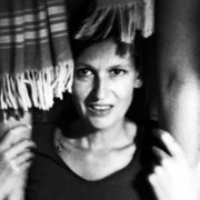 Frau mit kurzen Haaren, umgeben von handgefertigten Textilien und Stoffen, die kreative und nachhaltige Handwerkskunst repräsentieren.