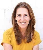 Lächelnde Frau mit braunen Haaren und blauen Augen trägt gelbes T-Shirt, steht vor weißer Wand, symbolisiert kreative Handwerkskunst und Handmade Kultur.