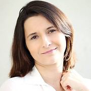 Freundliches Porträt einer Frau mit braunen Haaren, die einen weißen Blazer trägt, für Handmade Kultur, Fokus auf Handarbeit, Kreativität und Inspiration.