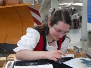 Frau arbeitet an einem handgefertigten Projekt in einer Werkstatt, umgeben von Werkzeugen und Materialien, zeigt handwerkliches Geschick und kreative Gestaltung.