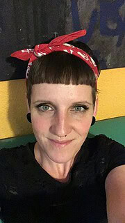 Frau mit Kurzhaarschnitt, roter Bandana, lächelnd, kreative Handarbeit, Kunsthandwerk, DIY, handgemacht, künstlerisch, individuelle Gestaltung, Handwerkskunst, kreative Inspiration.