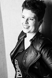 Schwarz-weiß Porträt einer lächelnden Frau mit kurzen Haaren, Lederjacke und Earring, die kreative und handgemachte Kultur repräsentiert.