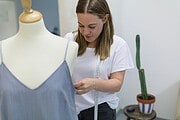 Frau misst ein handgefertigtes Kleidungsstück in einem Atelier, um die Passform zu prüfen, mit Fokus auf nachhaltige Mode und kreative Textilkunst.