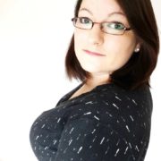 Frau mit dunklem Haar, Brille und schwarzem Oberteil mit weißen Linien, lächelnd und selbstbewusst, für Handmade Kultur SEO optimiert.