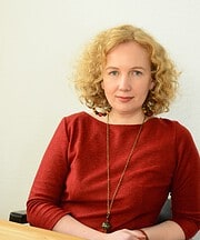 Frau mit lockigem blondem Haar trägt rotes Oberteil und Schmuck, zeigt kreative Handwerkskunst für Handmade Kultur, Fokus auf Kunsthandwerk und kreative Gestaltung.