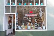 Stoffladen mit großen Schaufenster, kreative Dekorationen, Nähzubehör und handgemachte Produkte, einladend für Kunden, die handgefertigte Stoffe und Nähbedarf suchen.