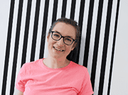 Lächelnde Frau mit Brille vor schwarz-weißen Streifenhintergrund, symbolisiert kreative Handwerkskunst und nachhaltige Kultur bei Handmade Kultur.