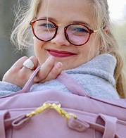 Lächelndes Mädchen mit runden Brille, grauem Hoodie und pinkem Rucksack, zeigt Freude und Kreativität, passend für Handmade Kultur Themen.