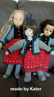 Drei handgefertigte Stoffpuppen mit gestrickten Kleidern und Jacken, ideal für Dekoration oder Spielzeug, präsentiert auf einer Couch, kreative Handarbeit von Kater.
