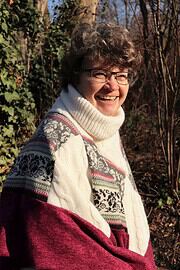 Lächelnde Frau trägt einen handgestrickten Wollpullover mit traditionellen Mustern, umgeben von Natur im Freien, bei Tageslicht, für Handmade Kultur.