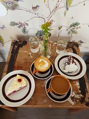 Tisch mit Kaffee, zwei Kuchenstücken, Wasser und einer kleinen Vase mit Blumen, gemütliches Ambiente für eine Kaffeepause.
