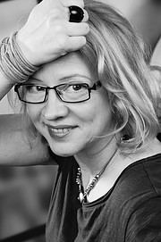 Frau mit Brille, lockigem Haar und Schmuck, die kreativ arbeitet, symbolisiert Handmade Kultur und kreative Handwerkskunst.
