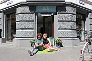 Zwei Frauen sitzen vor dem Eingang von HANDMADE Kultur, einem Kreativstudio in Berlin, umgeben von Blumen, mit einem Fahrrad im Hintergrund, das kreative Handwerkskunst fördert.