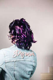 Modische Lockenfrisur in Lila- und Violetttönen, getragen mit einer hellblauen Denim-Jacke mit Stickerei "stay real" auf dem Rücken, für kreative Handwerks- und Modeinspiration.