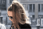Frau mit Sonnenbrille und lockigem Haar, die in einer urbanen Umgebung unterwegs ist, symbolisiert kreativen und nachhaltigen Lifestyle im Rahmen von Handmade Kultur.